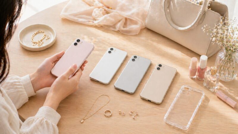 白やベージュや淡いピンクのスマホと小物を合わせて選ぶ女性の手元
