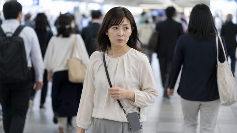 混雑した駅でスマホショルダーの危険性を意識する日本人女性