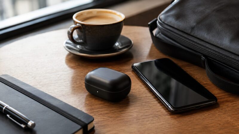 カフェのテーブルに置かれた黒いワイヤレスイヤホンケースと日用品