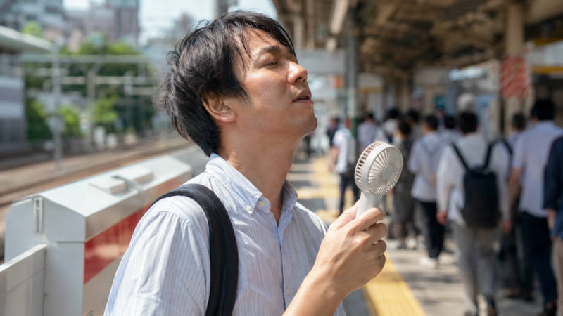 真夏の駅でハンディファンのターボ運転を使う日本人