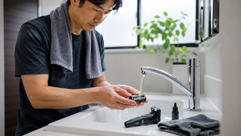 電気シェーバーの外刃を流水で洗浄する日本人男性