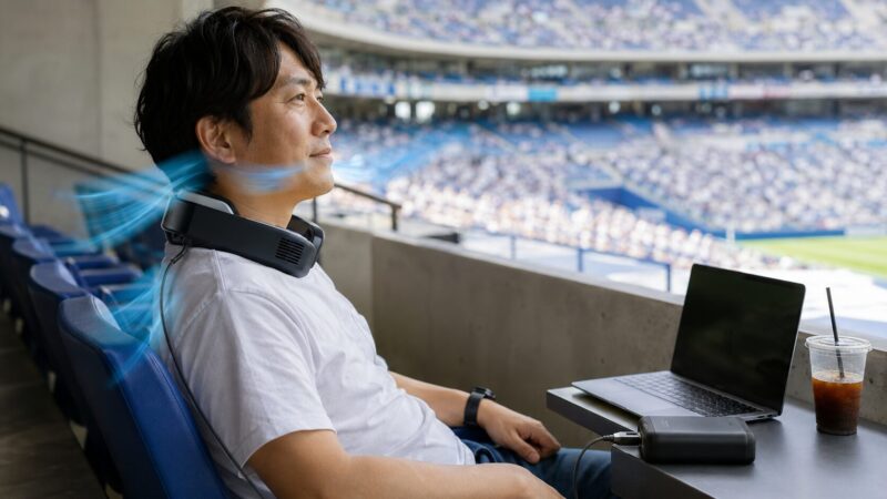 送風機能付きネッククーラーを外部電源につないで観戦席で使う日本人男性