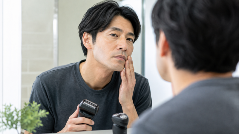 電動シェーバーで剃った頬の仕上がりと肌の状態を確認する日本人男性